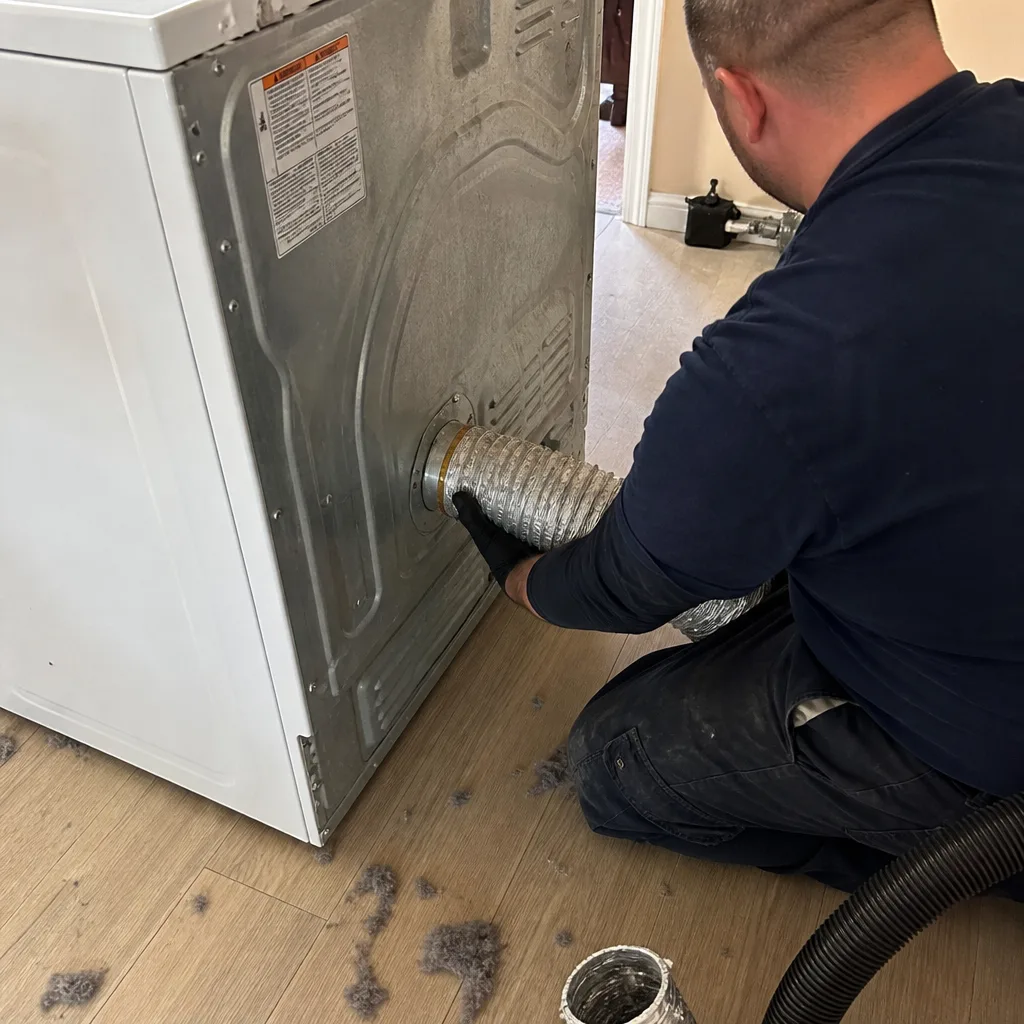Professional technician cleaning a residential dryer vent duct with a vacuum hose